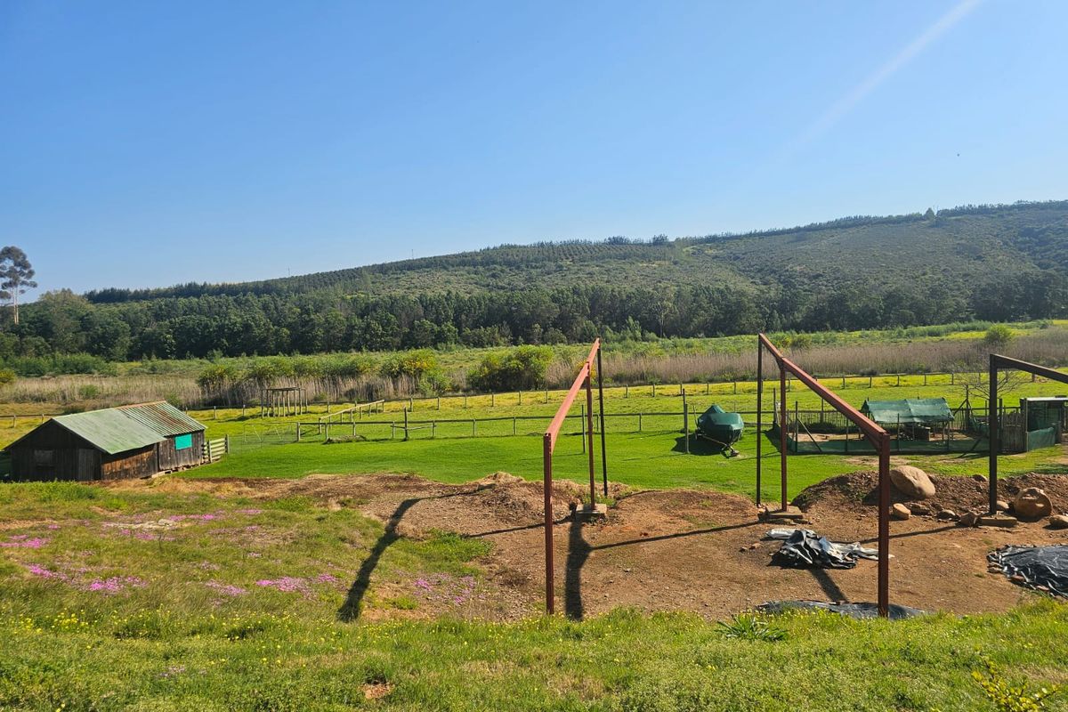 Expansive farm landscape featuring a wooden shed, perimeter fencing, and an unfinished metal structural frame set against a scenic hillside backdrop.
