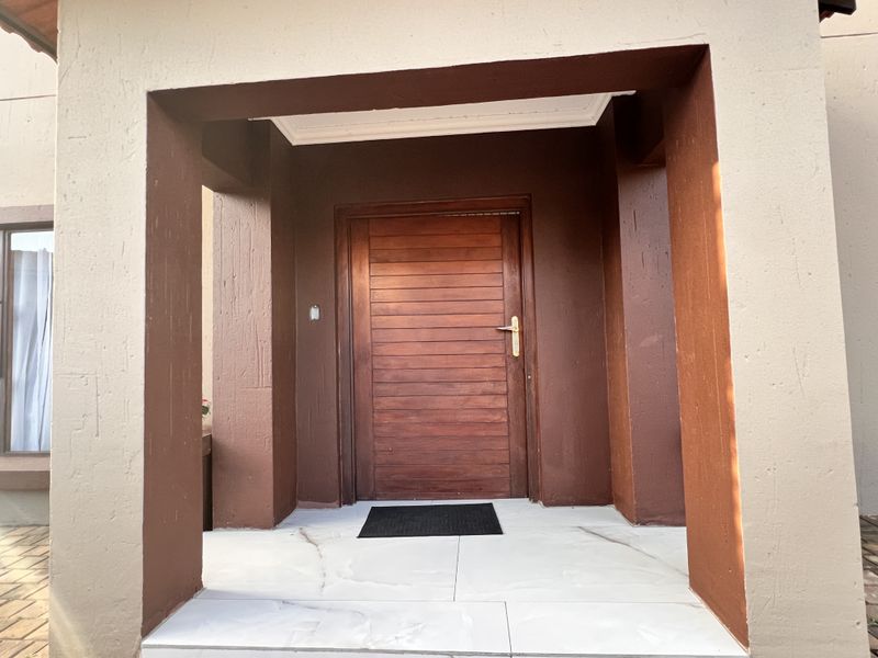 A covered front entrance featuring a solid wood door and modern light-colored porcelain floor tiles.