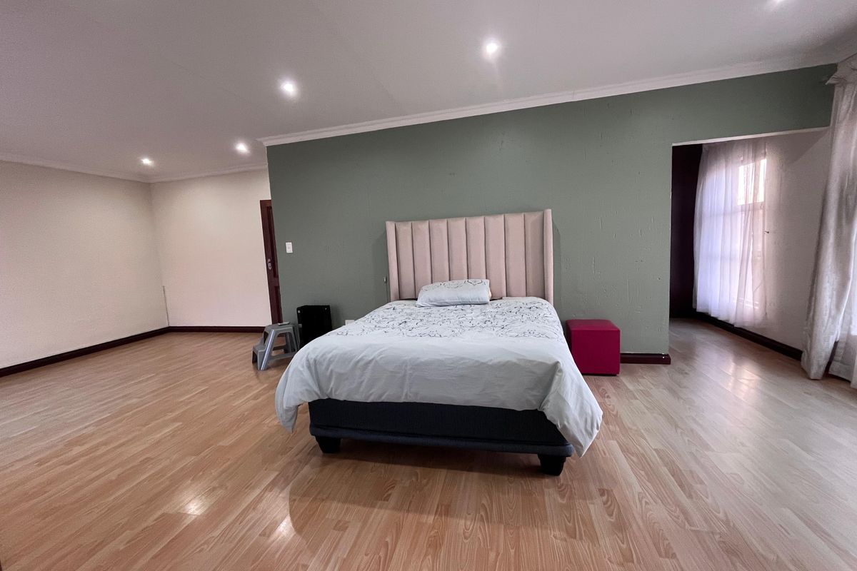 Spacious bedroom featuring light wood-look laminate flooring, recessed downlighting, and a feature wall, offering a neutral canvas for interior design updates.