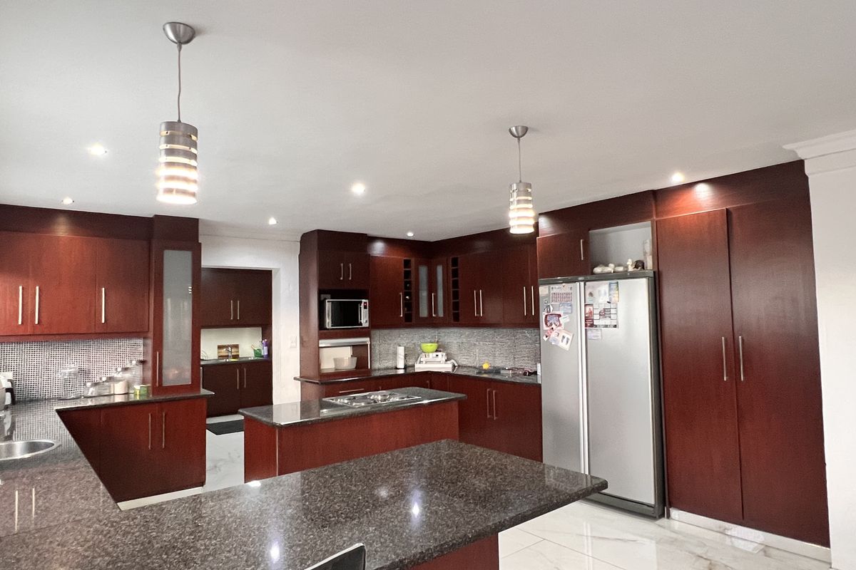 Spacious kitchen featuring dark wood cabinetry, granite countertops, a central island with a hob, and modern pendant lighting with tiled flooring.