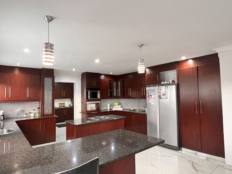 Spacious kitchen featuring dark wood cabinetry, granite countertops, a central island with a hob, and modern pendant lighting with tiled flooring.