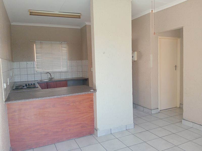 A functional kitchen area featuring built-in cabinetry, a hob, sink, and tiled splashback, presented in a clean, empty space ready for updates.