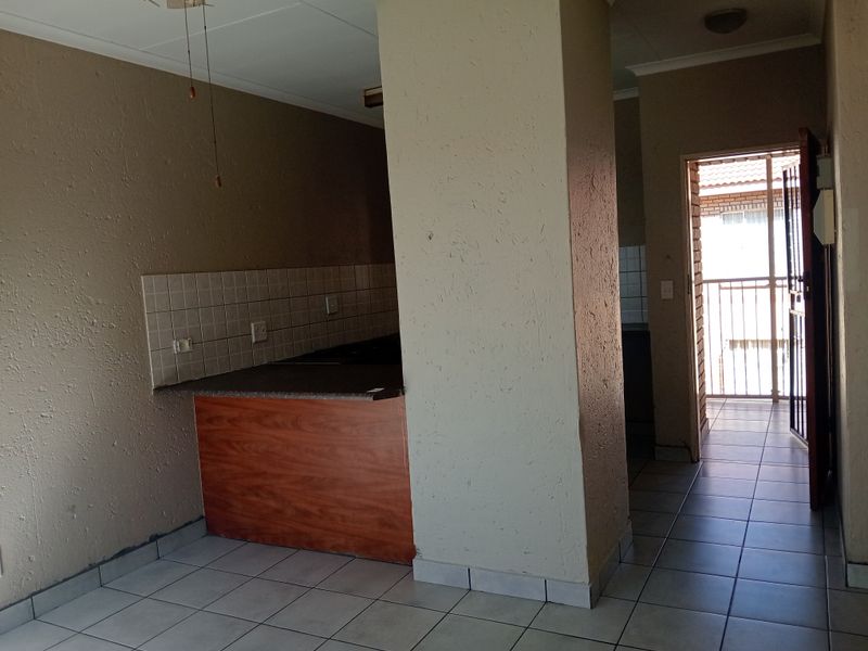 An empty open-plan living and kitchen area featuring tiled flooring, a built-in counter, and direct access to an exterior balcony through a security gate.
