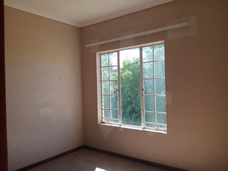 An empty bedroom featuring a steel-framed window, carpeted flooring, and coving, currently requiring cosmetic wall repairs and fresh paint.