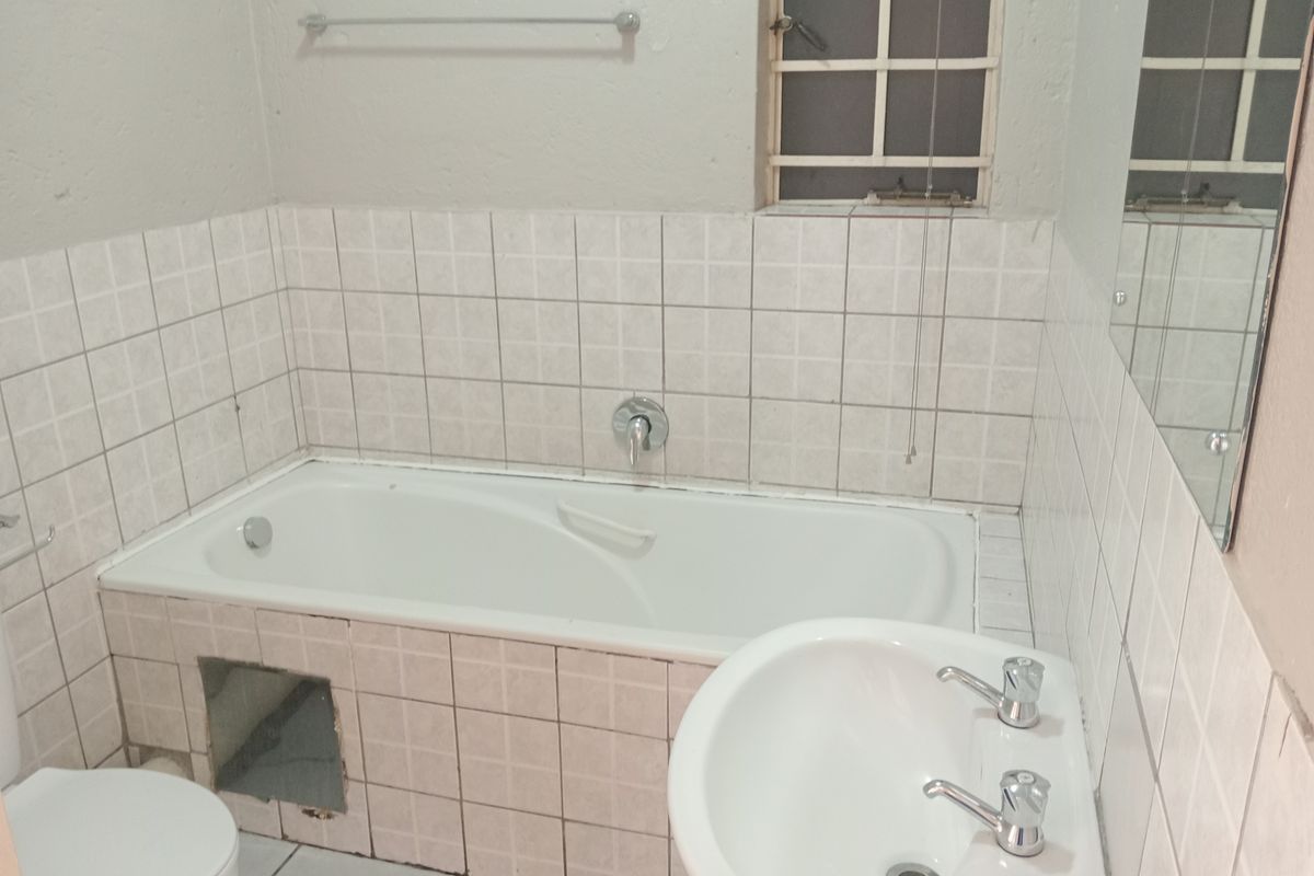 A functional bathroom featuring a bathtub, pedestal basin, and tiled splashback, requiring minor repairs to the bathtub apron and general cosmetic updates.