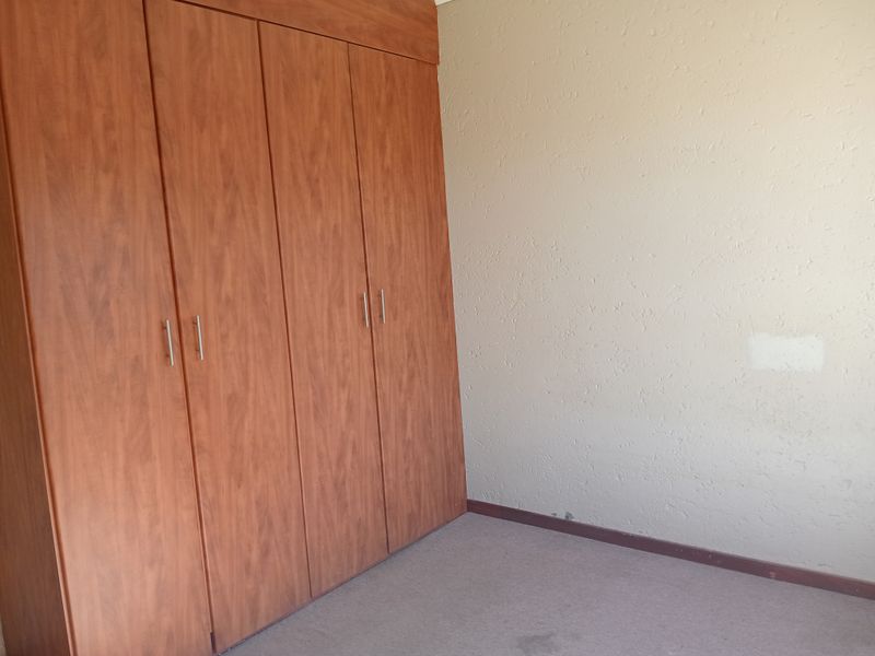 An empty bedroom featuring a large built-in wooden wardrobe, textured walls, and carpeted flooring.