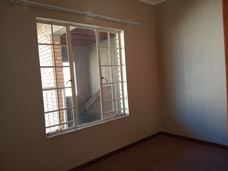 An empty bedroom featuring a steel-framed window, neutral wall paint, and carpeted flooring, ready for renovation or staging.
