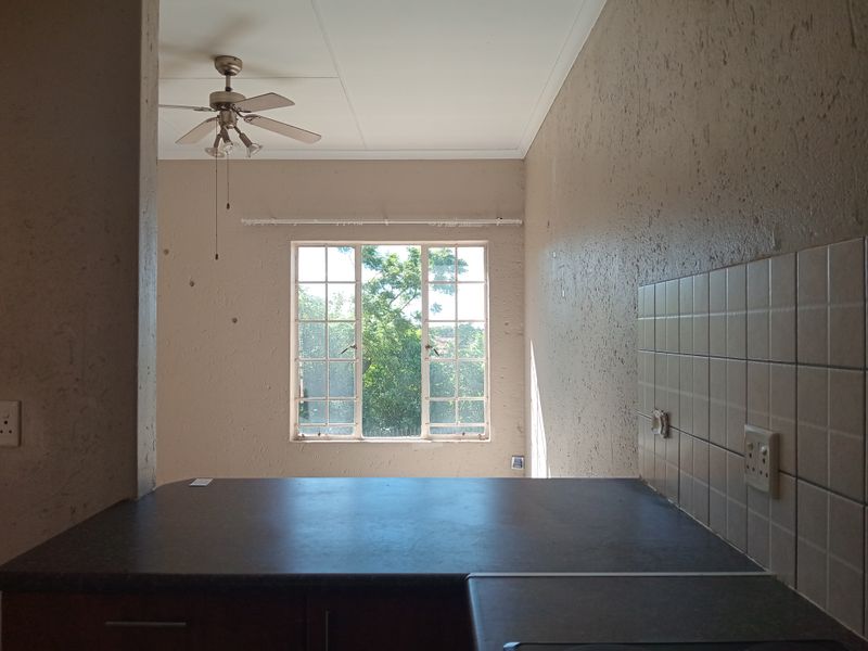 An empty kitchen area featuring a dark laminate countertop, tiled backsplash, and a ceiling fan, with a window providing natural light.