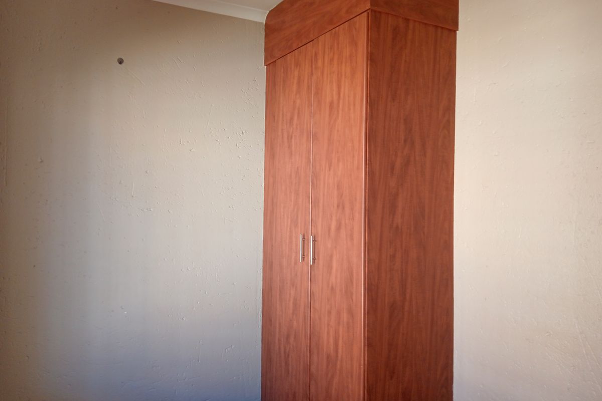 A bedroom featuring a built-in wooden wardrobe with a top bulkhead, set against plain walls with coving.
