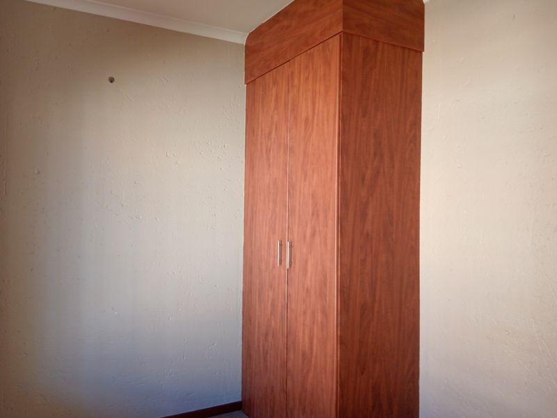 A bedroom featuring a built-in wooden wardrobe with a top bulkhead, set against plain walls with coving.