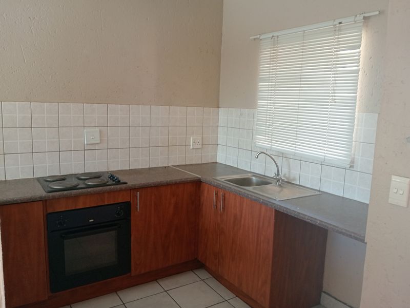 A functional kitchen featuring wood-veneer cabinetry, a built-in oven with electric hob, stainless steel sink, and tiled splashback, ready for a modern update.