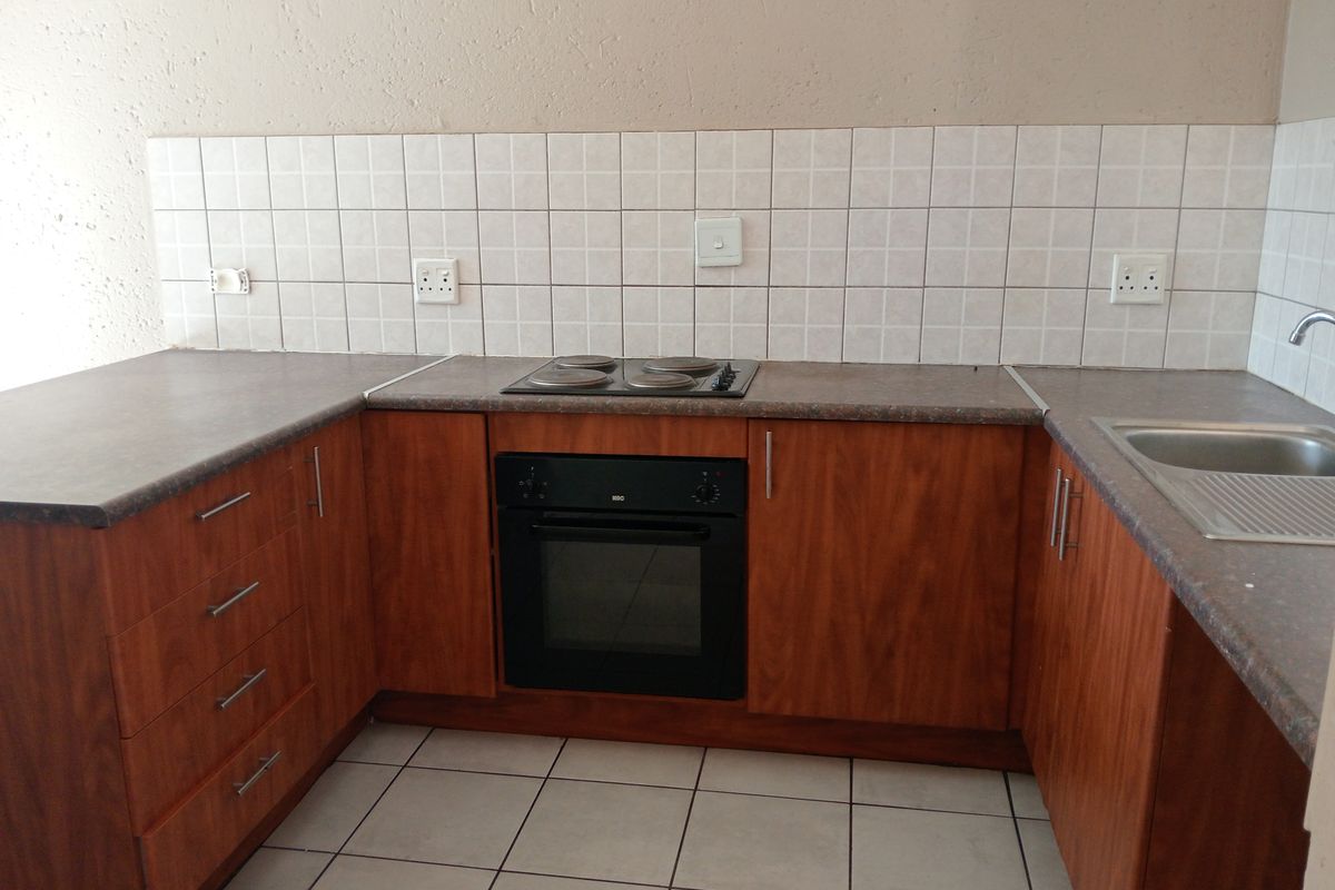 A functional kitchen featuring wooden cabinetry, laminate countertops, a built-in oven with electric hob, and tiled flooring with a neutral backsplash.