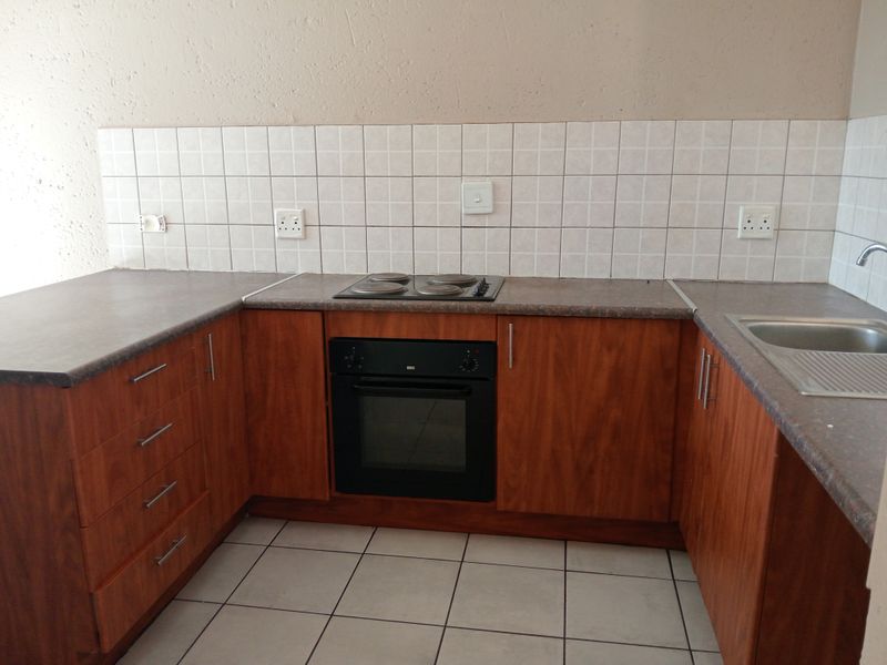 A functional kitchen featuring wooden cabinetry, laminate countertops, a built-in oven with electric hob, and tiled flooring with a neutral backsplash.