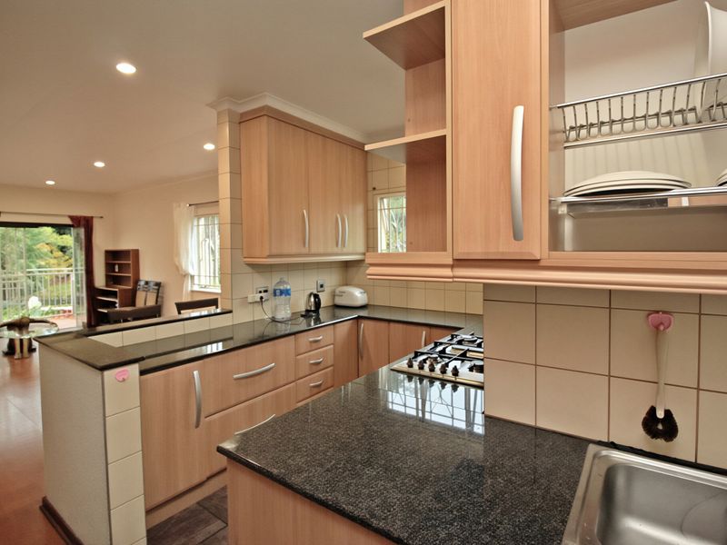 Open-plan kitchen featuring granite countertops, light wood cabinetry, and a gas hob, flowing seamlessly into a living area with access to a balcony.