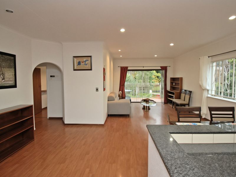 Spacious open-plan living area featuring laminate flooring, recessed lighting, and a granite-topped kitchen counter, with direct access to a balcony through sliding glass doors.