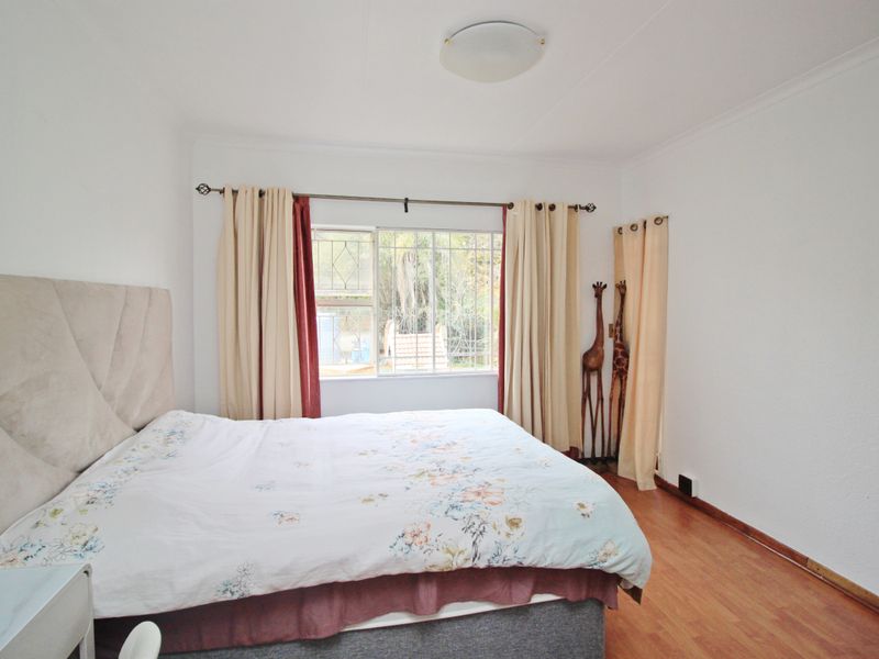 A bedroom featuring laminate flooring, a window with security bars, and a ceiling light fixture.
