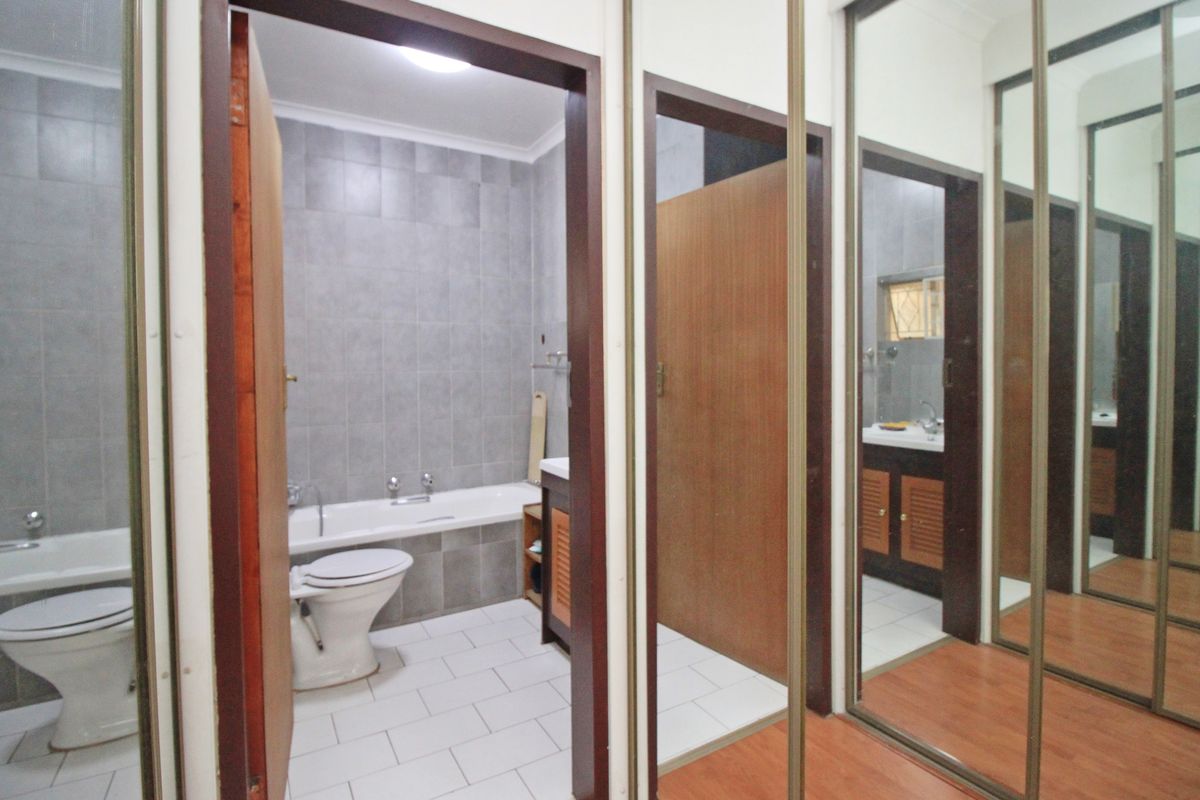 A functional bathroom featuring tiled walls and flooring, a built-in vanity, and a bathtub, adjacent to a hallway with mirrored sliding wardrobe doors.