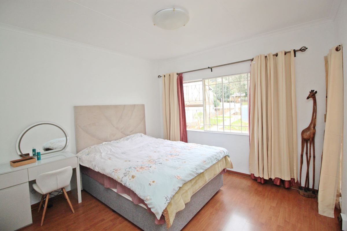 A bedroom featuring laminate flooring, a window with security bars, and a central ceiling light fixture.