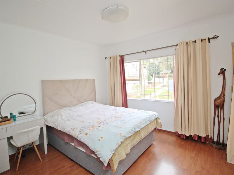 A bedroom featuring laminate flooring, a window with security bars, and a central ceiling light fixture.