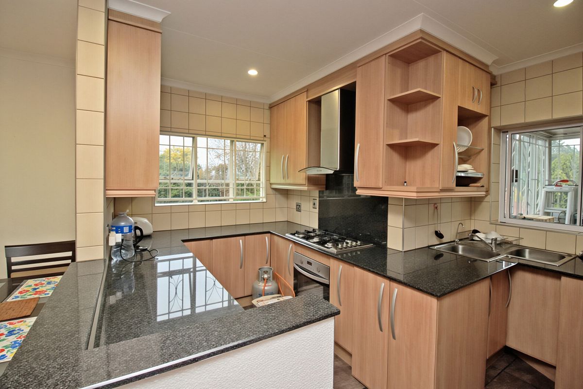 Functional kitchen featuring granite countertops, built-in oven, gas hob, extractor fan, and ample fitted cabinetry with tiled splashbacks.