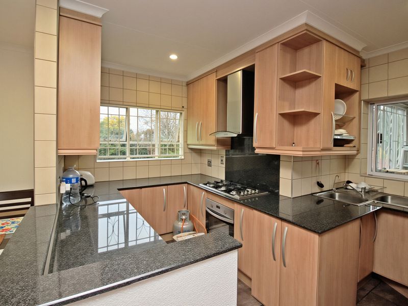 Functional kitchen featuring granite countertops, built-in oven, gas hob, extractor fan, and ample fitted cabinetry with tiled splashbacks.