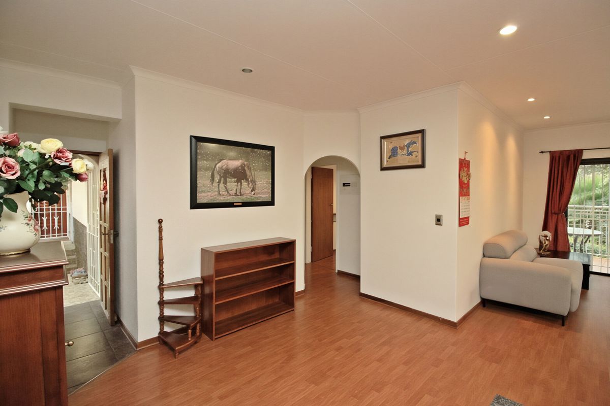 A living area featuring laminate flooring, recessed lighting, and an arched doorway leading to an adjacent space, with access to an outdoor balcony.