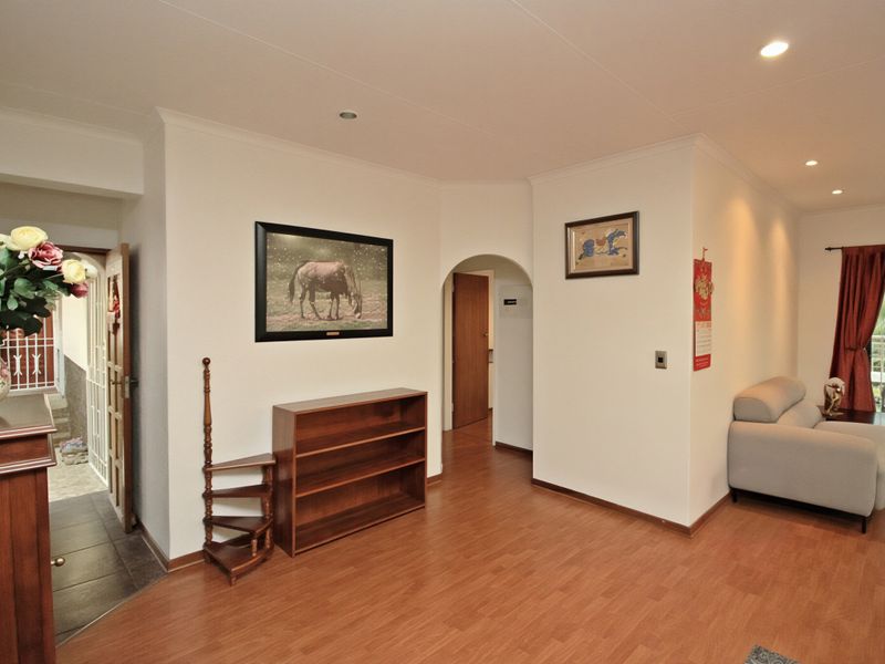 A living area featuring laminate flooring, recessed lighting, and an arched doorway leading to an adjacent space, with access to an outdoor balcony.