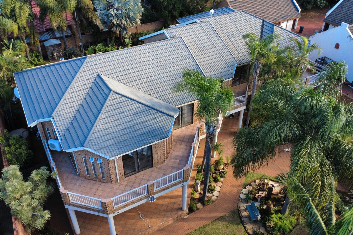Aerial view of a residential property featuring a tiled roof, elevated patio area, and landscaped garden with paved walkways.