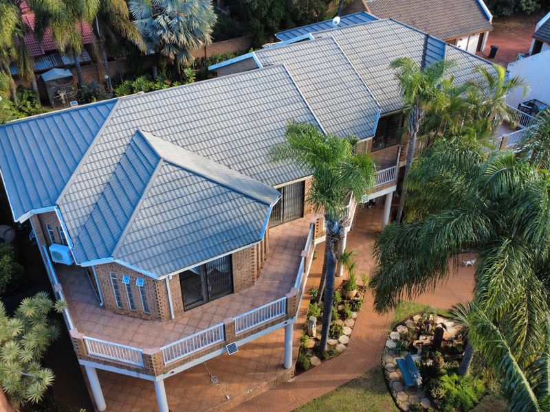 Aerial view of a residential property featuring a tiled roof, elevated patio area, and landscaped garden with paved walkways.