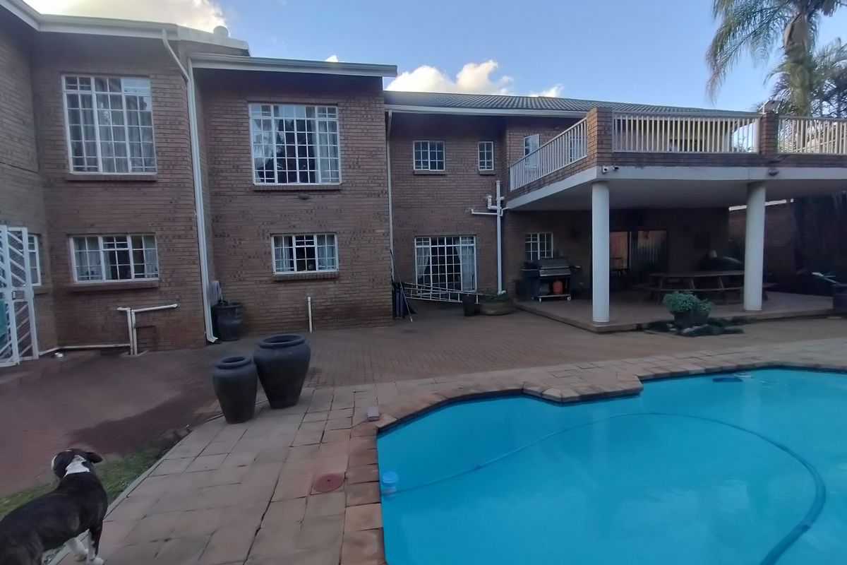 Rear view of a double-story brick house featuring a swimming pool, paved patio area, and an elevated balcony.