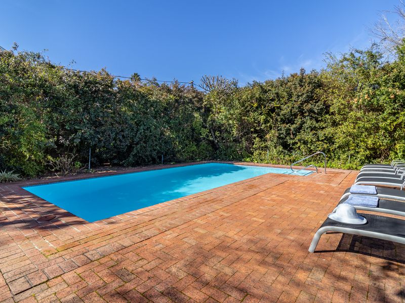 A private outdoor swimming pool area featuring a brick-paved deck surrounded by mature, dense perimeter hedging.