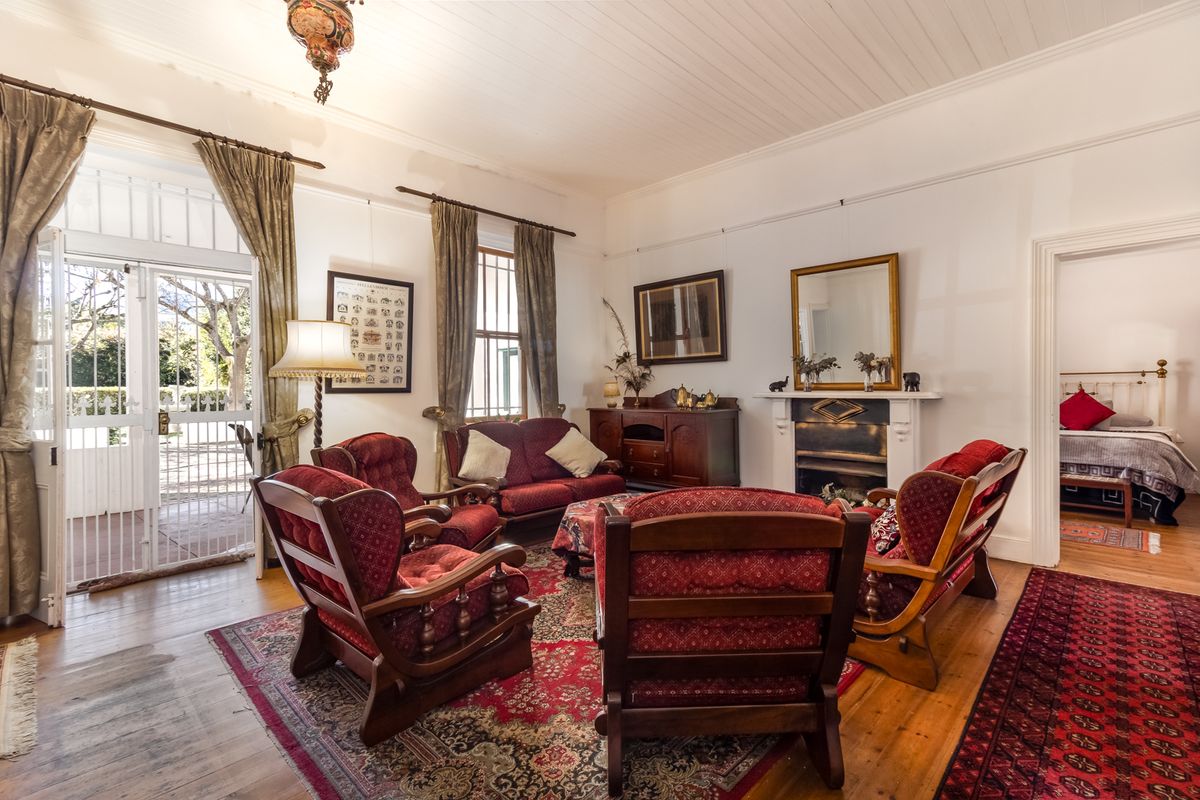 A character-filled living room featuring original timber flooring, a classic fireplace mantel, and direct access to an outdoor patio area.