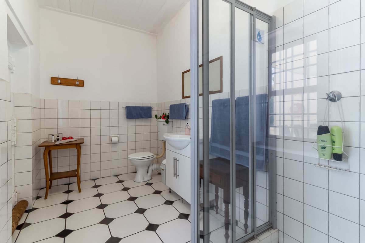 A functional bathroom featuring a shower enclosure, pedestal vanity, and toilet, finished with classic black and white patterned floor tiles and wall tiling.