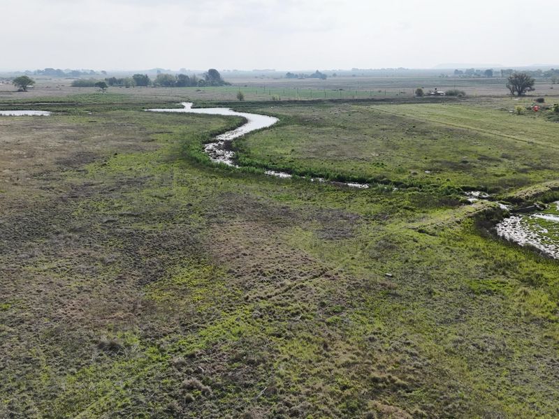 An aerial view of the expansive farm property featuring a natural winding stream and open grazing pasture land.