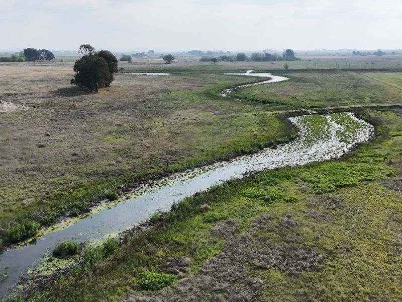 An aerial view of the expansive farm property featuring a natural winding watercourse flowing through open pasture land.