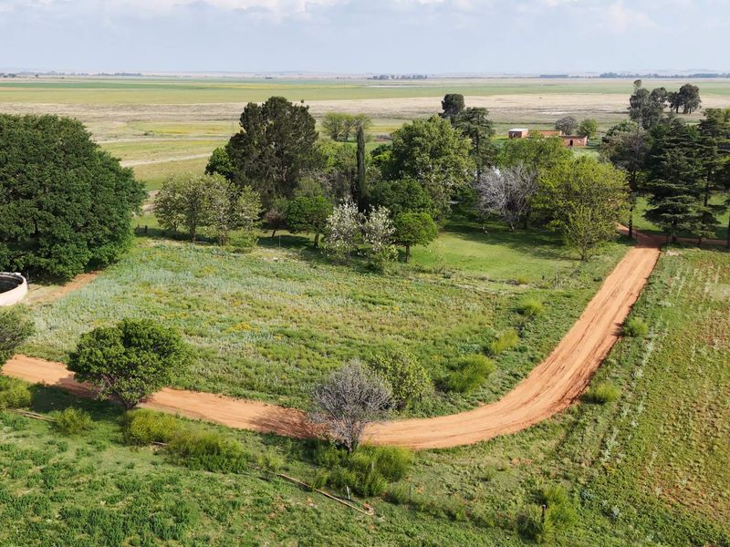 Aerial view of the farm property featuring a dirt access road, established trees, and a circular water reservoir set within open grazing land.