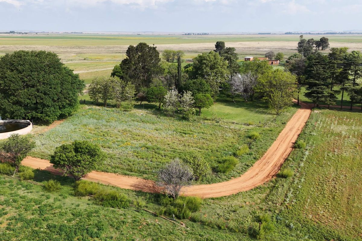 Aerial view of the farm property featuring a dirt access road, established trees, and a circular water reservoir set within open grazing land.
