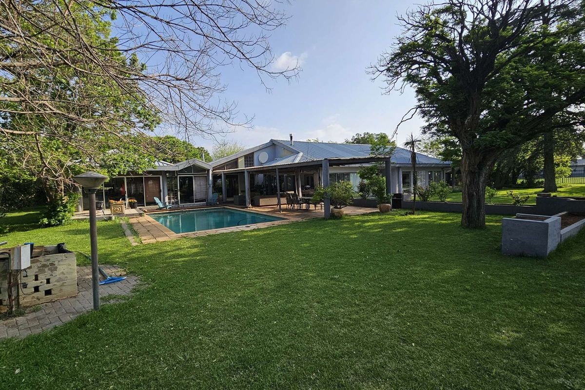 Rear view of the farm property featuring a swimming pool, covered patio area, and expansive lawn with mature trees.