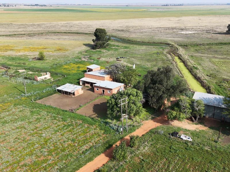 Aerial view of a rural farm property featuring multiple outbuildings, fenced enclosures, and an irrigation canal set within expansive agricultural land.