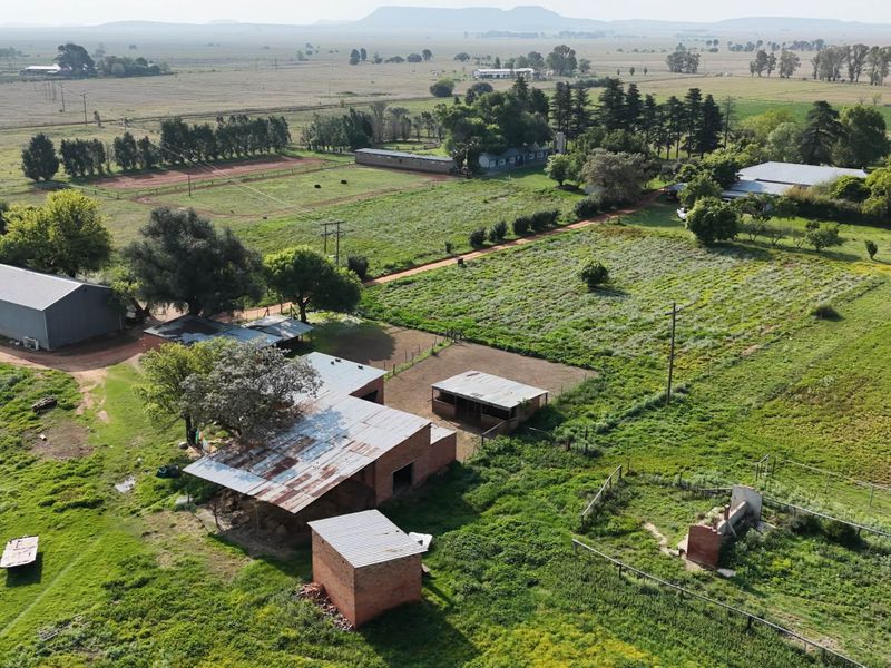 Aerial view of a farm property featuring multiple outbuildings, corrugated metal roofing, and expansive surrounding agricultural land.