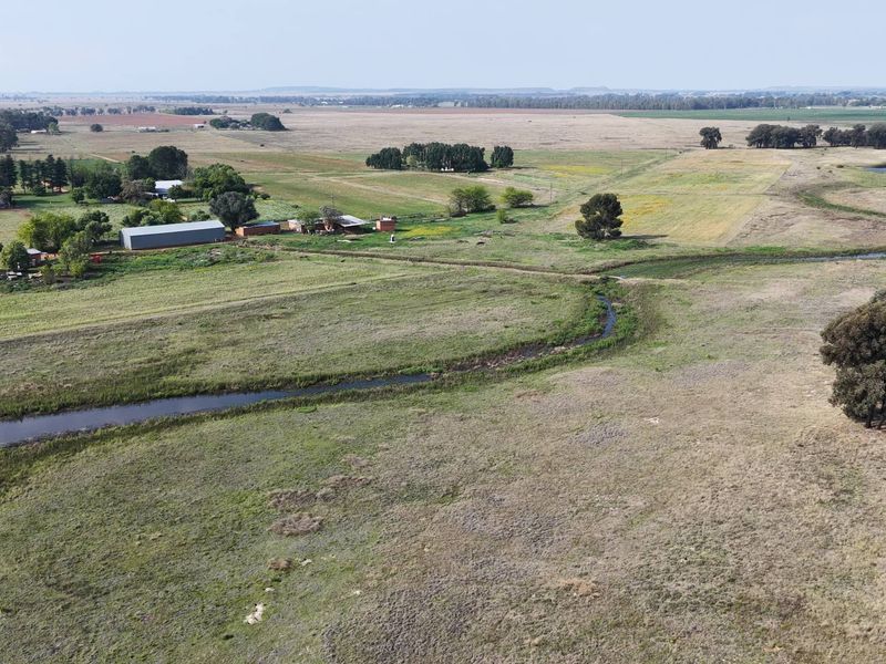 An aerial view of the expansive farm property featuring open grazing land, a natural water stream, and existing outbuildings.