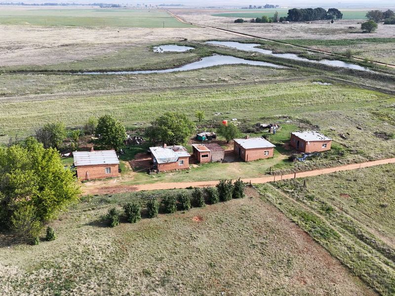 Aerial view of a rural farm property featuring multiple detached brick buildings with corrugated metal roofs set within a large open landscape.