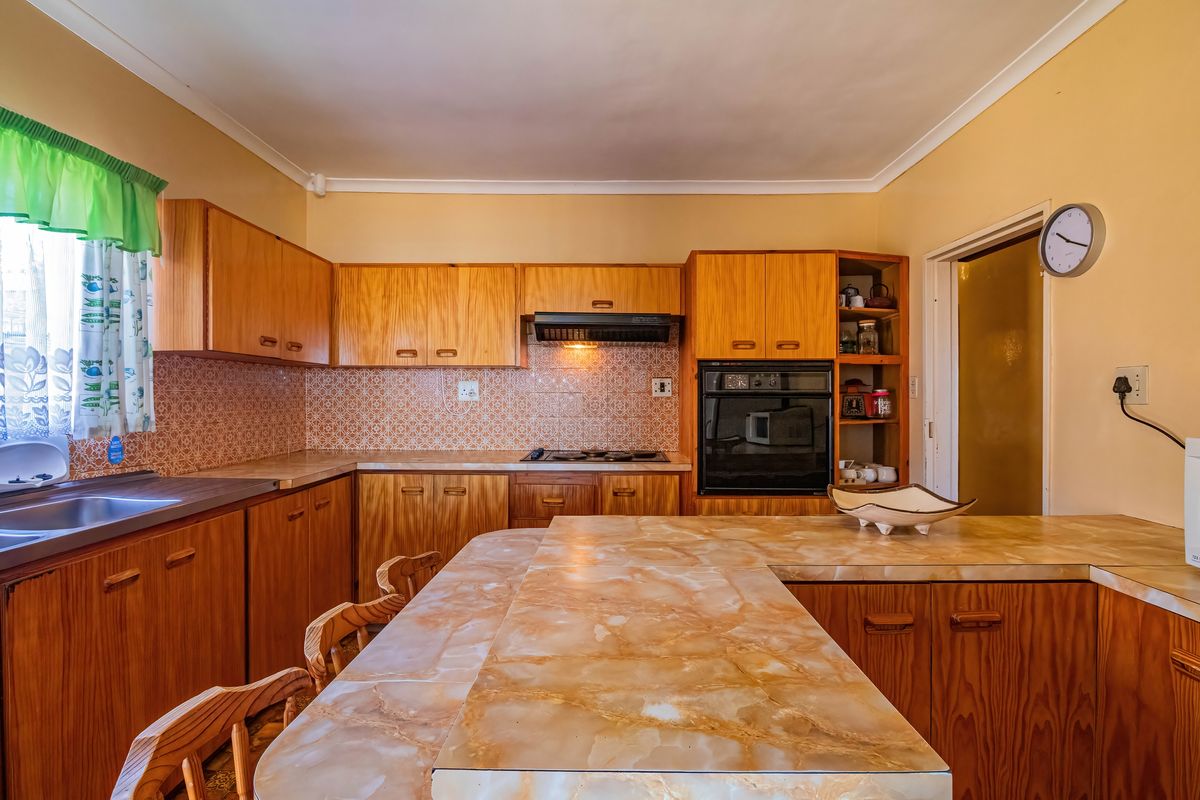 A functional kitchen featuring wooden cabinetry, built-in oven, hob, extractor fan, and tiled backsplash with a breakfast counter.