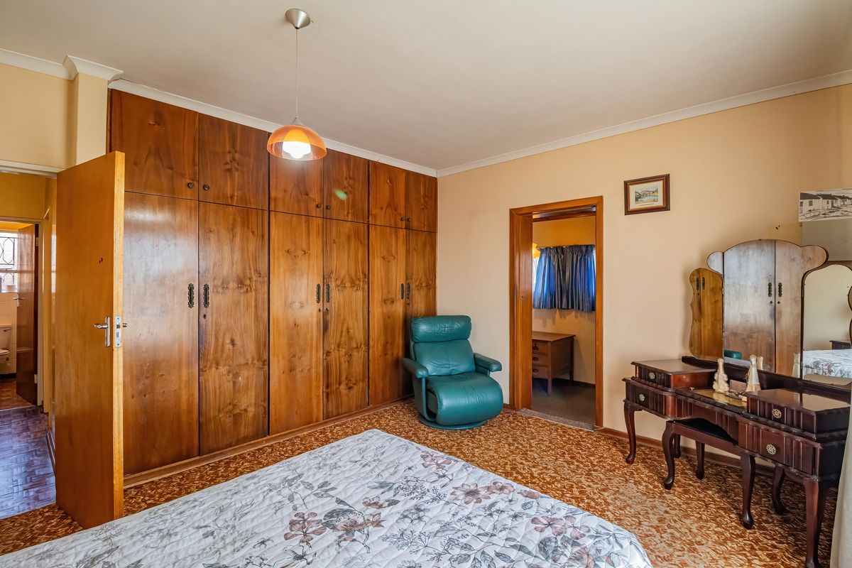 A bedroom featuring extensive built-in wooden cabinetry, cove cornicing, and carpeted flooring, offering a traditional layout with an adjacent room access.
