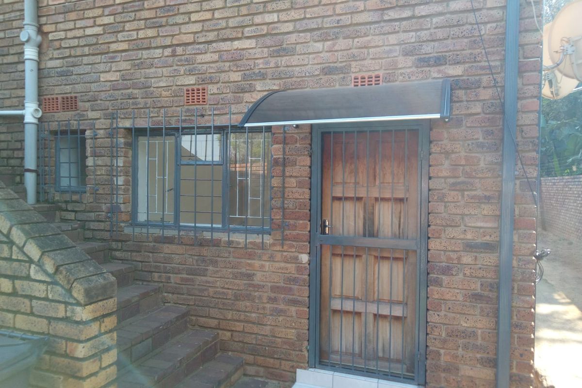Rear exterior view of the apartment featuring a face brick facade, security bars on windows, and a timber entrance door with a protective awning.