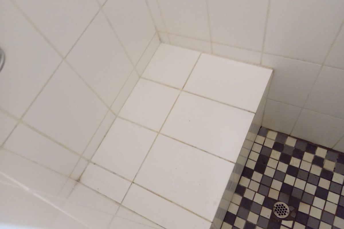 A close-up view of a tiled shower enclosure featuring a built-in bench seat and a mosaic floor drain.