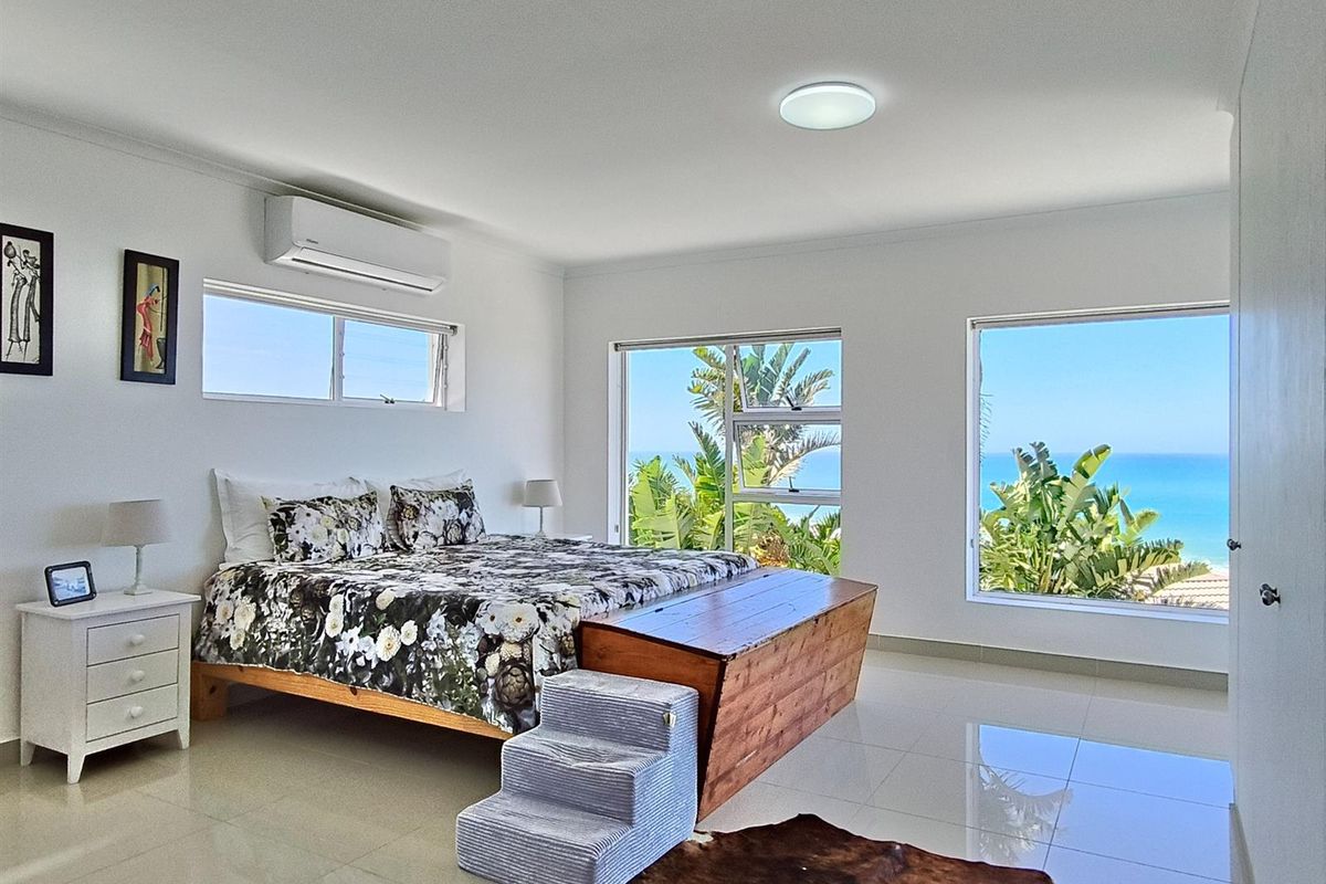 Spacious bedroom featuring large windows with ocean views, tiled flooring, and a wall-mounted air conditioning unit.