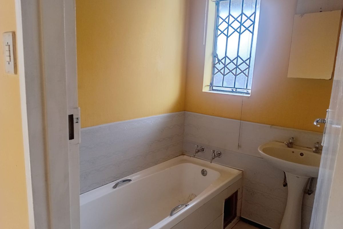 A dated bathroom featuring a built-in bathtub, pedestal basin, and security-fitted window, requiring cosmetic updates to improve its overall condition and appeal.