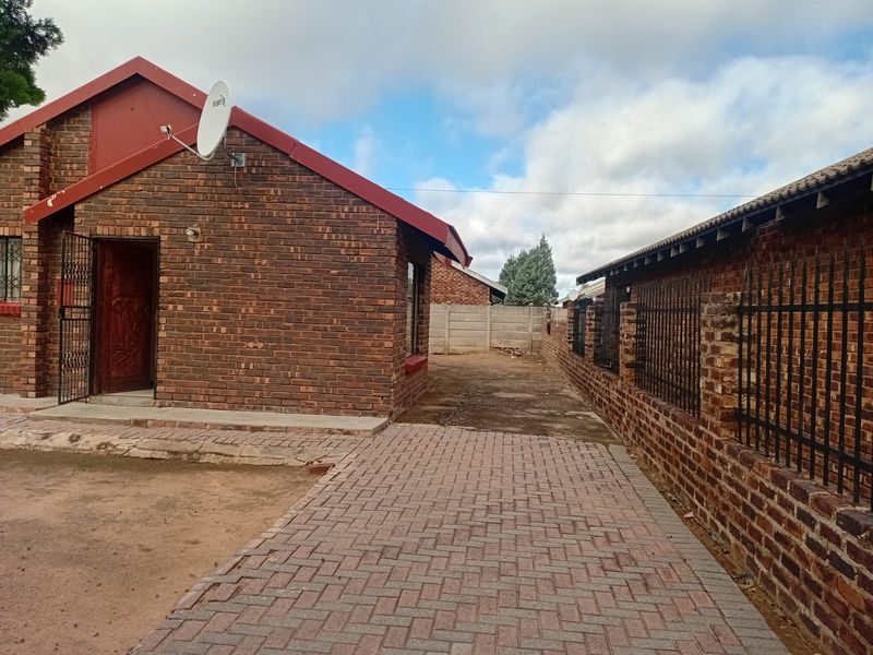 A view of the front exterior of a face brick house featuring a paved driveway, security gate, and perimeter walling.
