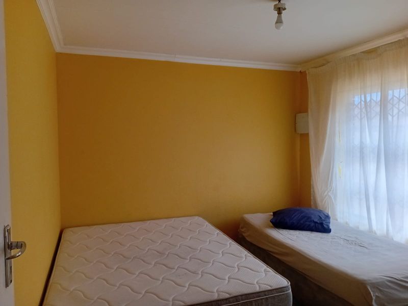 A simple bedroom featuring yellow walls, a cornice, and a window fitted with a security gate.